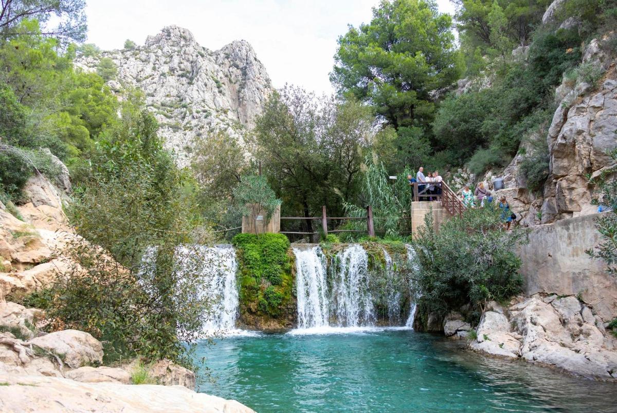 a waterfall in a canyon with people standing in front of it