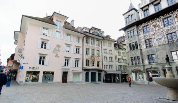 Cobblestone square with painted facades, a fountain, a 'KIKO' boutique and a small outdoor café at KoBi Apartments Hirschenplatz in Luzern