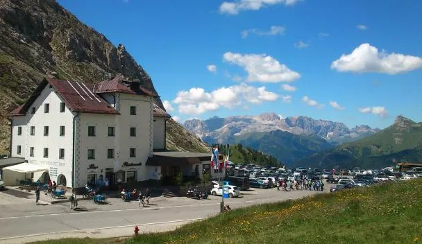 Hotel Ristorante with outdoor terrace and parking lot, mountain peaks and a cloud-filled blue sky in the background at Hotel Col di Lana in Canazei