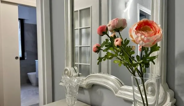 Ornate white mirror with silver trim, vase of pink flowers and crystal vase on dresser, bathroom with frosted glass door at Interno1 in Mestre