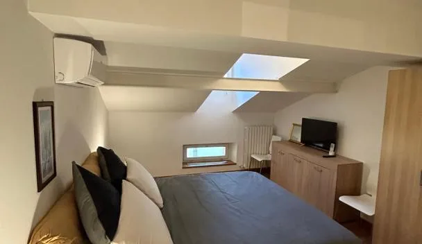 Attic double bedroom with skylight, low sloped ceiling, gray bedcover, bedside lamp, wall-mounted TV and wooden dresser at Appartamento centrale Housitaly in Lecco