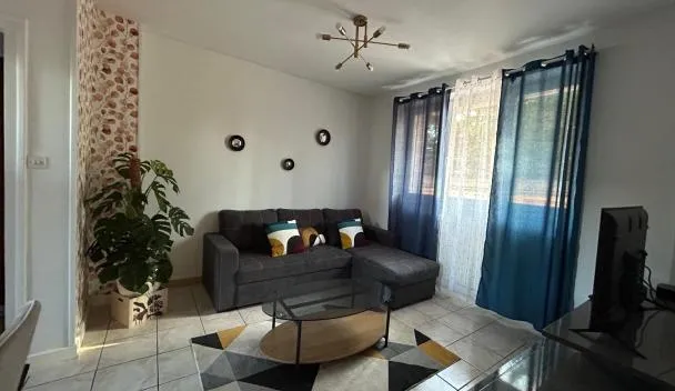 Living room with gray L-shaped sofa, glass coffee table, geometric rug, wall-mounted TV and floor-to-ceiling curtains at Home Lyla in Dijon