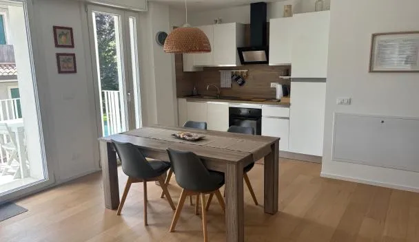 Open-plan kitchen and dining area with wooden table and four chairs, built-in oven and microwave, and balcony access at Cozy Corner Treviso Station #4 in Treviso