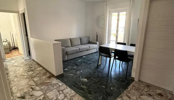 Open-plan living/dining with gray sofa, marble-effect terrazzo floor, four-seat dining table and balcony access at Riviera Comfort Homes 2 in Sanremo