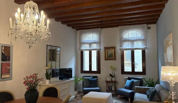 Open-plan living/dining with exposed wooden beams, crystal chandelier, three shuttered windows, sofa, TV and coffee table at SANTA CATERINA: charming apartment TREVISO in Treviso