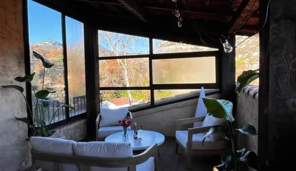 Covered terrace with cushioned armchairs, round table with wine glasses, potted plant and panoramic hillside view at L'Attrape-Rêves in La Gaude