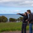 two people standing in a field pointing at the ocean