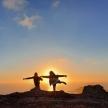 two people standing on top of a mountain at sunset