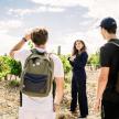 a group of people standing in a vineyard looking at a woman