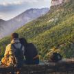 a couple sitting on a ledge looking at a mountain