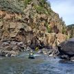 a person in a kayak in a river next to a mountain