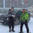 two people on skis in the snow in front of a car