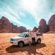two people standing next to a car in the desert