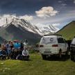 a group of people standing in a field next to two vans