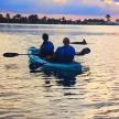 two people in a kayak on the water at sunset