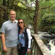 a man and a woman standing on a bridge in front of a waterfall