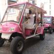 two people riding a pink golf cart on a street