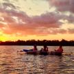 three people in a boat on a lake at sunset
