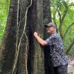 a man standing next to a tree in the woods