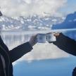 a man and woman holding coffee mugs in front of a lake