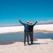 a man and woman standing on a beach with their arms up