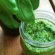 a glass jar filled with pesto next to a green plant