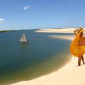 a woman in a yellow dress standing on a beach with a sail boat