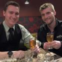 two men sitting at a table with glasses of beer