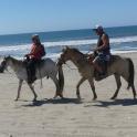 two people are riding horses on the beach