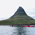 two people in red boats in the water with a mountain