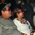 two older people sitting in an audience wearing sunglasses