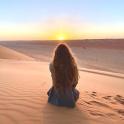 a woman sitting in the desert watching the sunset