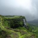 a moss covered cliff with a waterfall on a mountain