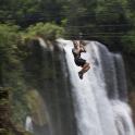 a man riding a zip line over a waterfall