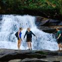 three people standing on rocks in front of a waterfall