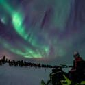 a person sitting on a snowmobile under the northern lights