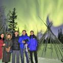 a group of people standing in the snow under the northern lights