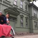 two men riding in a horse drawn carriage in front of a building