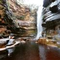 two people sitting on the rocks in front of a waterfall