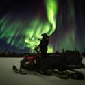 一个人站在极光下的雪地摩托上