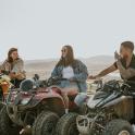 three people sitting on atvs in the desert