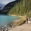 two people walking down a path next to a lake