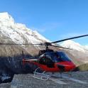 a red helicopter parked in front of a snow covered mountain