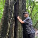 a man standing next to a tree in the woods
