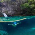 a person swimming in the water near a waterfall