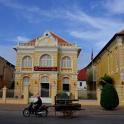 a person riding a motorcycle in front of a yellow building