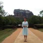 a woman standing on a dirt road with a mountain in the background