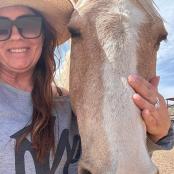 一位戴着牛仔帽的女人站在一匹马旁边