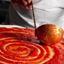 člověk maže omáčku na pizzu