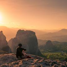 a man sitting on top of a mountain watching the sunset